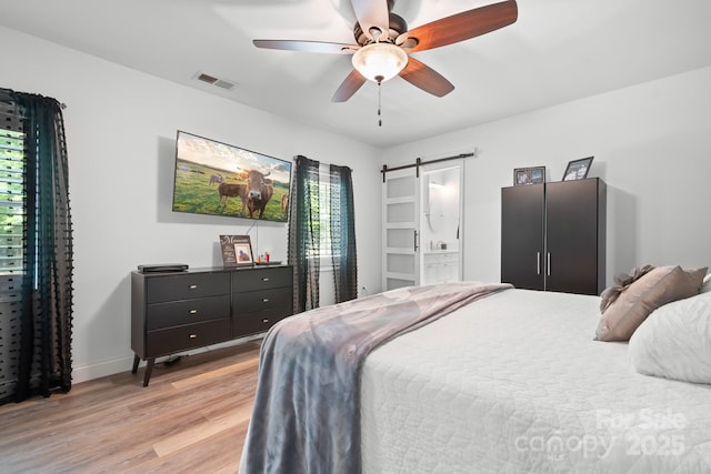 bedroom with a barn door, light wood-type flooring, baseboards, and ceiling fan