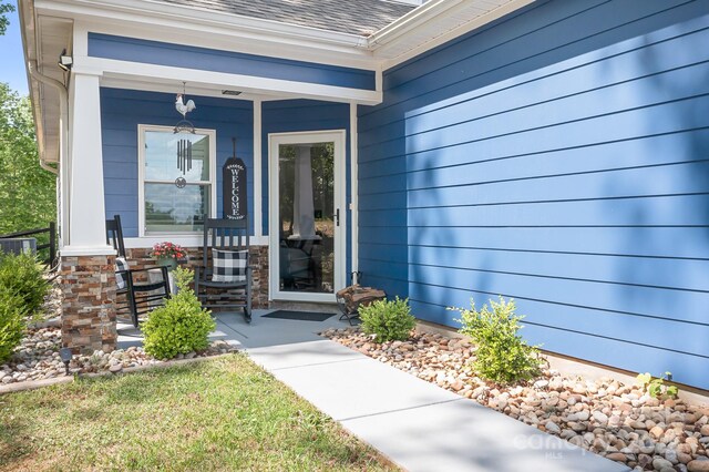doorway to property featuring covered porch and roof with shingles
