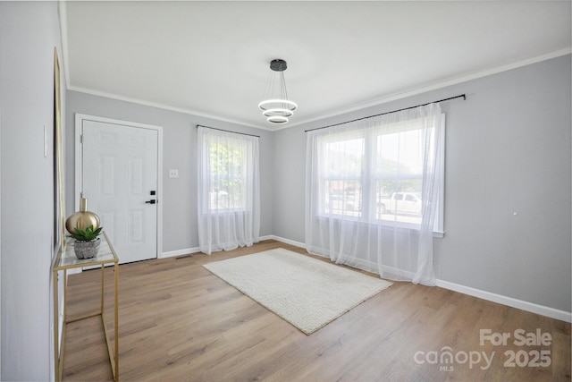 entrance foyer with light wood finished floors, an inviting chandelier, baseboards, and ornamental molding