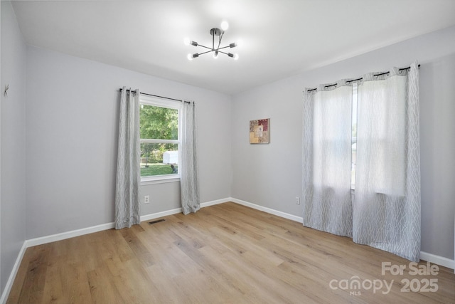 unfurnished room with baseboards, a notable chandelier, visible vents, and wood finished floors