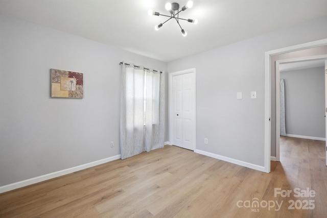 unfurnished bedroom with an inviting chandelier, light wood-type flooring, a closet, and baseboards
