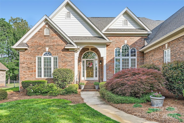 traditional home featuring brick siding, roof with shingles, and fence