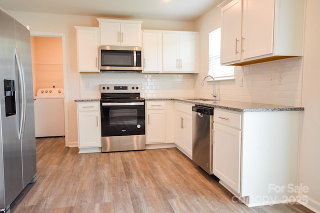 kitchen featuring a sink, white cabinets, washer / dryer, appliances with stainless steel finishes, and light stone counters