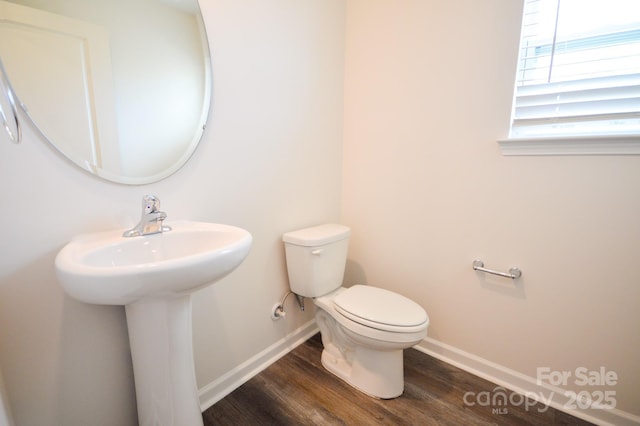 half bathroom with toilet, baseboards, a sink, and wood finished floors