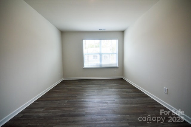 empty room featuring dark wood-style flooring, baseboards, and visible vents