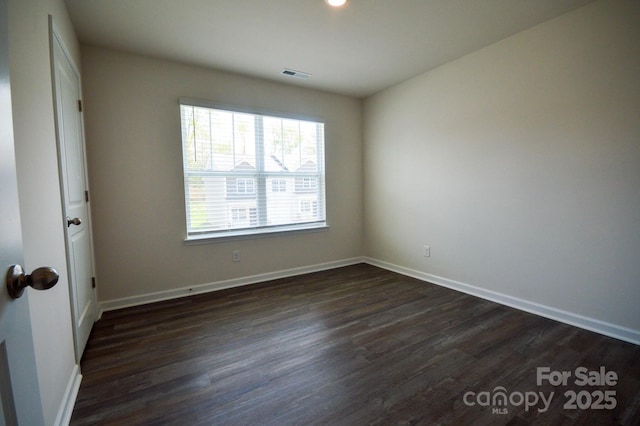 spare room featuring baseboards, dark wood finished floors, and visible vents