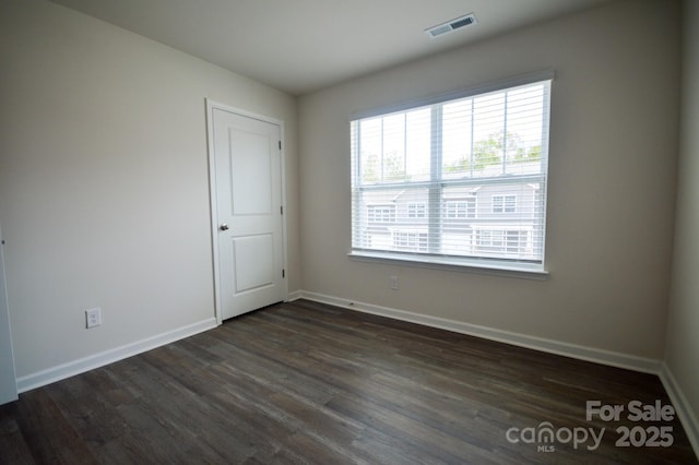 unfurnished room with dark wood finished floors, visible vents, and baseboards