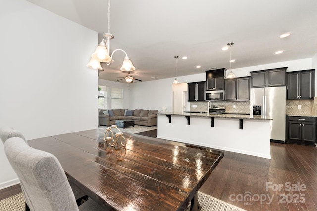 dining space featuring recessed lighting, ceiling fan with notable chandelier, and dark wood-type flooring