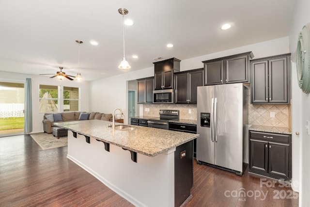 kitchen with a breakfast bar, a sink, a kitchen island with sink, dark wood-type flooring, and appliances with stainless steel finishes
