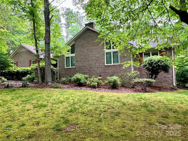 view of home's exterior with a chimney, brick siding, and a lawn