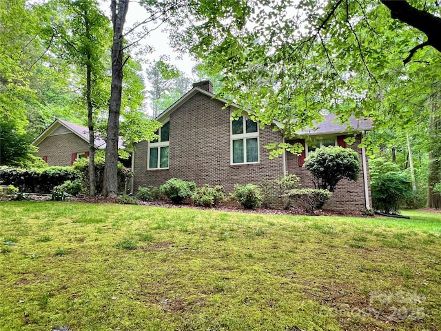 view of side of property with brick siding, a chimney, and a lawn