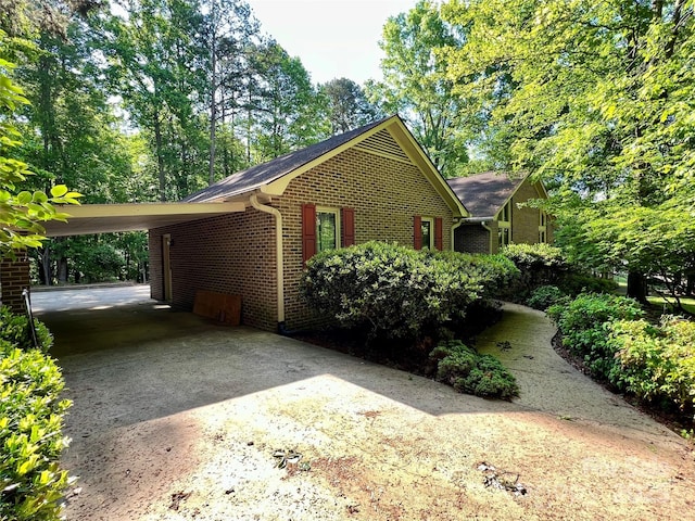 view of side of property with concrete driveway, brick siding, and a carport