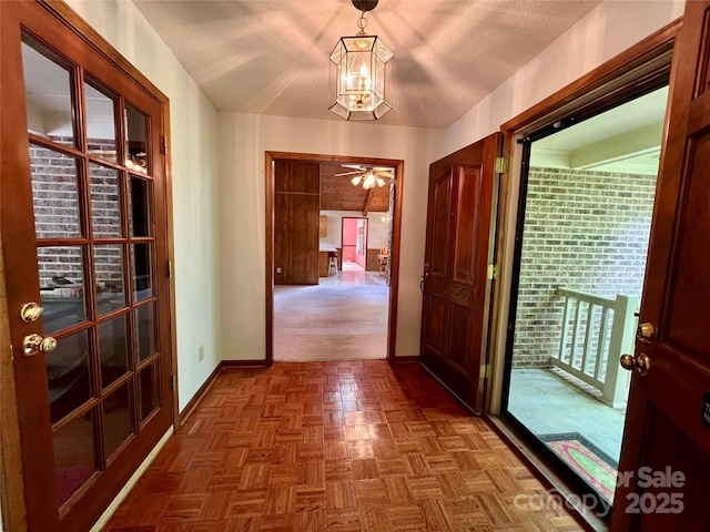 corridor featuring a textured ceiling, a chandelier, and baseboards
