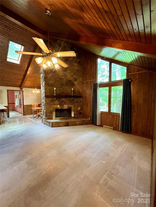 unfurnished living room featuring visible vents, lofted ceiling with skylight, ceiling fan, and wooden walls