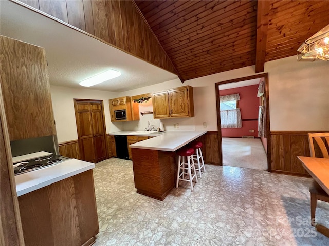 kitchen featuring a peninsula, cooktop, a wainscoted wall, stainless steel microwave, and light countertops