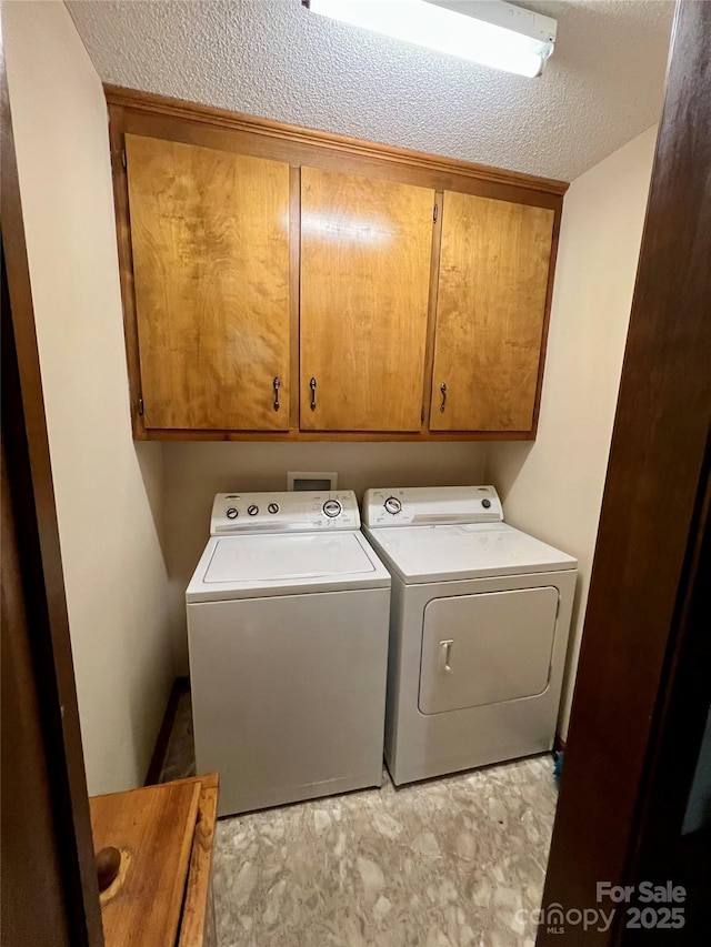 washroom featuring washer and clothes dryer, a textured ceiling, and cabinet space