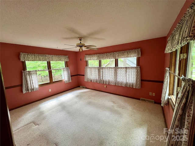carpeted empty room featuring a ceiling fan, baseboards, visible vents, and a textured ceiling