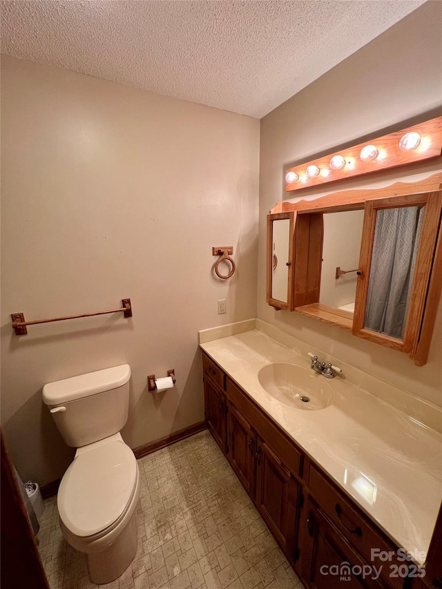bathroom with vanity, a textured ceiling, baseboards, and toilet