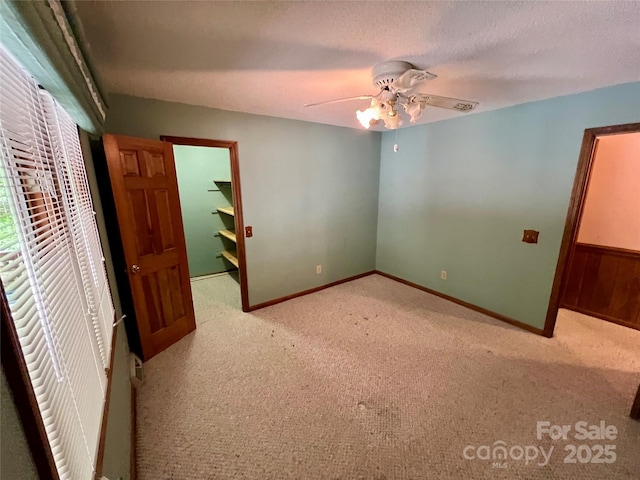 unfurnished bedroom with a closet, carpet, baseboards, ceiling fan, and a spacious closet