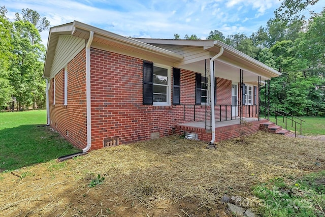 view of side of property with covered porch, crawl space, a yard, and brick siding