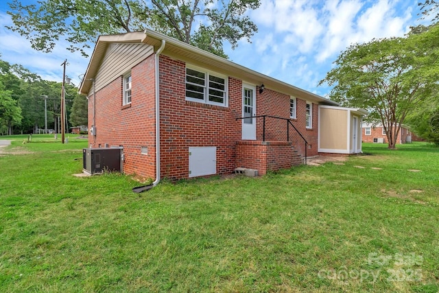 back of house featuring central air condition unit, a yard, and brick siding