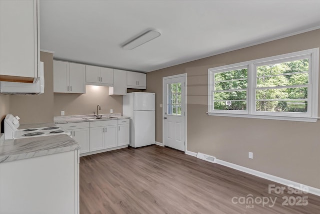 kitchen with white appliances, a sink, light countertops, white cabinets, and wood finished floors