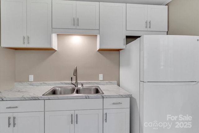 kitchen featuring freestanding refrigerator, a sink, white cabinetry, and light countertops