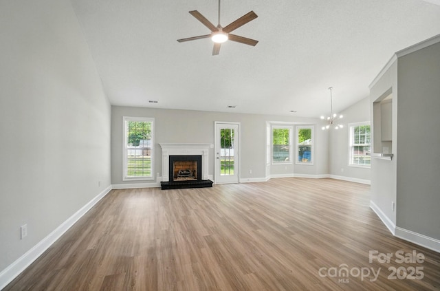 unfurnished living room with vaulted ceiling, a fireplace with raised hearth, ceiling fan, wood finished floors, and baseboards