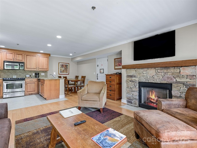 living room featuring recessed lighting, baseboards, light wood finished floors, crown molding, and a fireplace