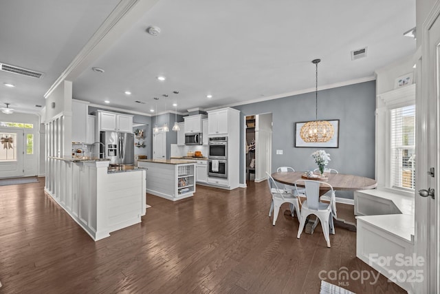 9871 Travertine Trl, Davidson, NC 28036 - kitchen featuring appliances with stainless steel finishes, ornamental molding, a center island, dark wood finished floors, and white cabinets