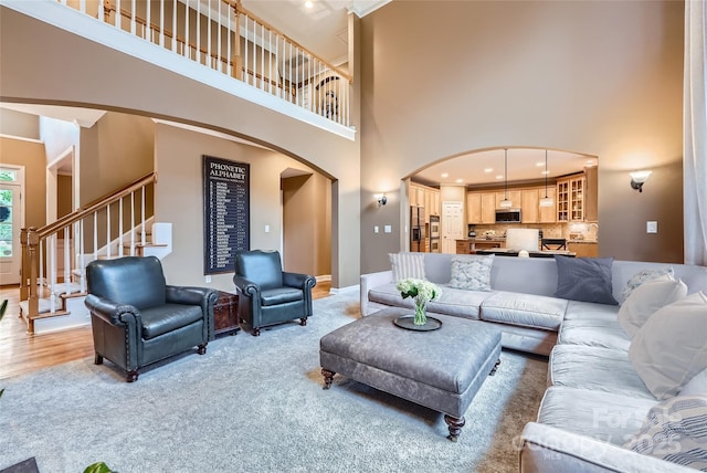 living room featuring light colored carpet, stairway, a towering ceiling, and arched walkways
