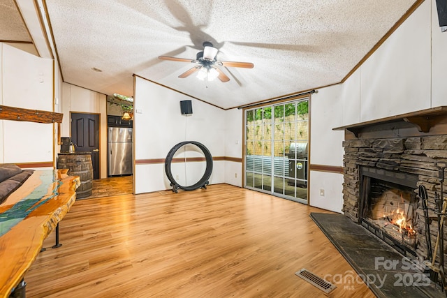 15 Robin Ln, Asheville, NC 28806 - living area featuring a textured ceiling, a ceiling fan, vaulted ceiling, a stone fireplace, and light wood-style floors