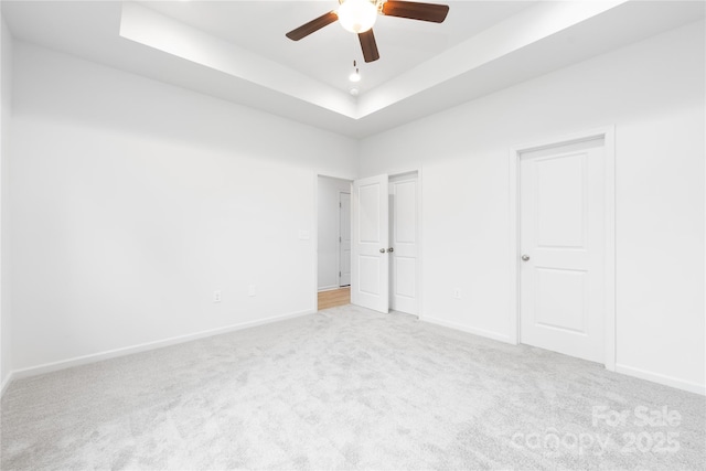 unfurnished bedroom with a raised ceiling, carpet flooring, baseboards, and a ceiling fan