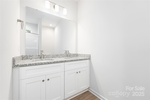 full bath featuring a sink, wood finished floors, visible vents, double vanity, and baseboards