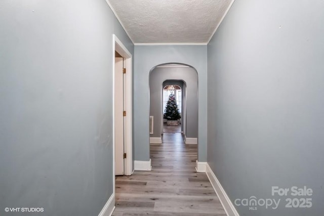 corridor with a textured ceiling, baseboards, arched walkways, and light wood-style floors