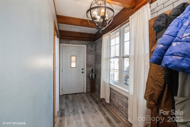 doorway to outside featuring a notable chandelier, light wood-type flooring, a healthy amount of sunlight, and beam ceiling