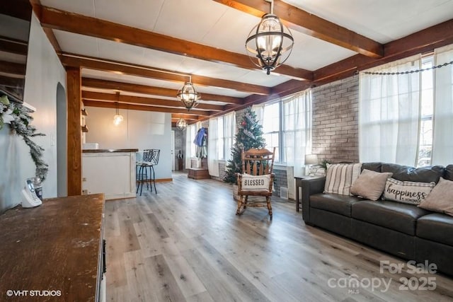 living room with beam ceiling, a chandelier, wood finished floors, and arched walkways