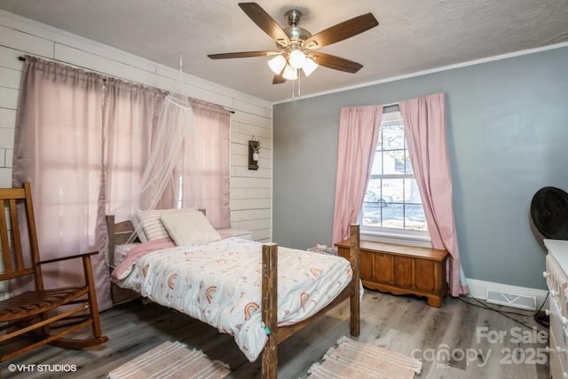 bedroom with wood finished floors, a ceiling fan, visible vents, baseboards, and ornamental molding
