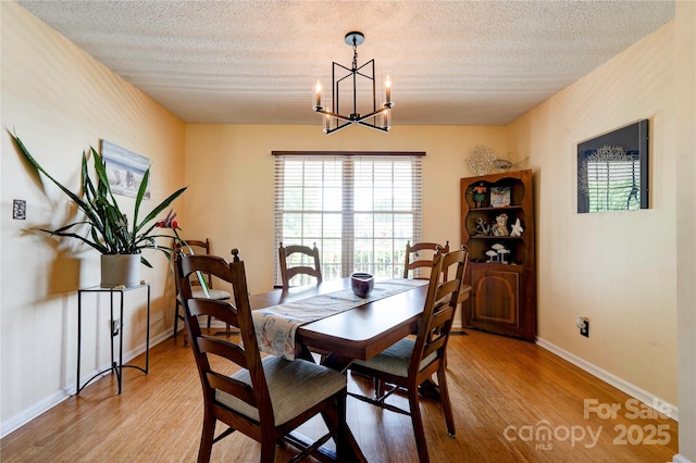 dining room with light wood finished floors, an inviting chandelier, a textured ceiling, and baseboards