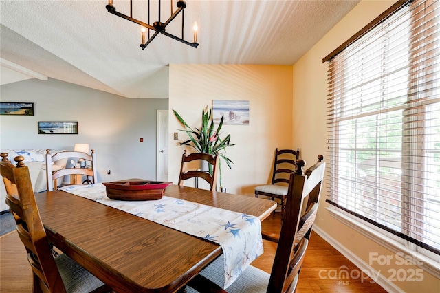 dining area featuring an inviting chandelier, plenty of natural light, vaulted ceiling, and light wood-style flooring