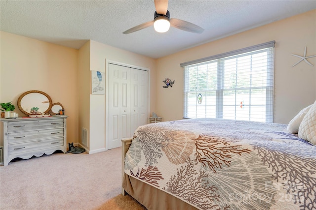 carpeted bedroom with a closet, a textured ceiling, visible vents, and ceiling fan