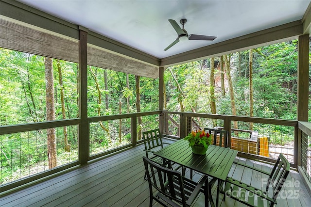 sunroom with ceiling fan, outdoor dining area, and a view of trees