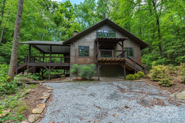 view of front of house with stairway, a wooden deck, a chimney, and a forest view