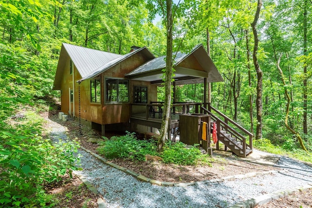 view of property exterior with stairs, a chimney, metal roof, crawl space, and a wooded view