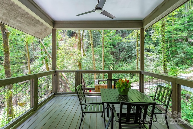 sunroom / solarium featuring ceiling fan, a view of trees, and outdoor dining space