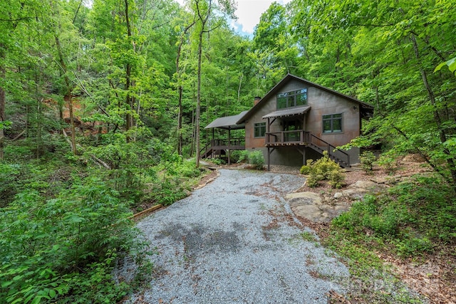 rustic home featuring a wooded view, a deck, stairs, and a chimney