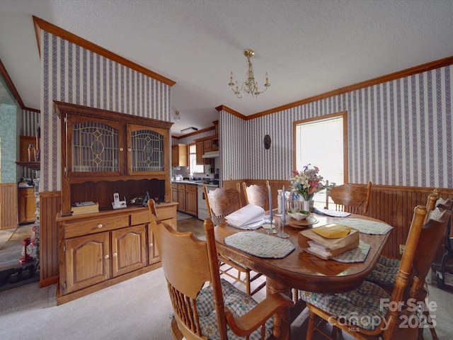 dining area with wallpapered walls, a textured ceiling, a chandelier, crown molding, and a wainscoted wall