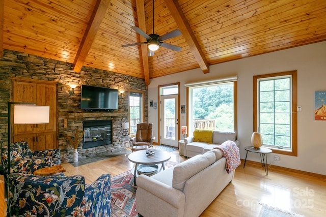living area with ceiling fan, a wealth of natural light, wood finished floors, and a stone fireplace