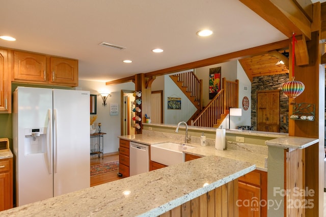 kitchen featuring a sink, recessed lighting, dishwasher, white refrigerator with ice dispenser, and light stone countertops