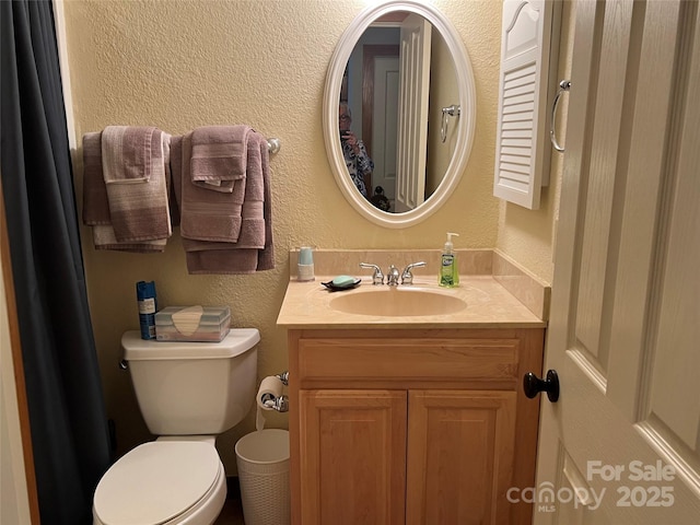 bathroom with toilet, vanity, and a textured wall